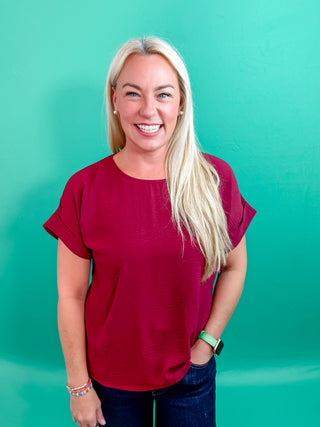 Burgundy Classic round neck short roll-up sleeve pullover top. Single button keyhole closure at back. Unlined. Woven. Non-sheer. Lightweight.
