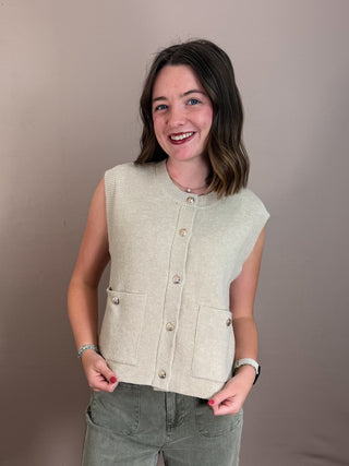 Solid sweater knit vest top featuring gold accent button closure at front. Pockets at front. Unlined. Knit. Non-sheer. Lightweight.