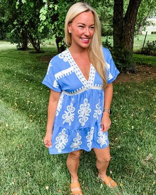 Blue and white printed mini dress with embroidered v-neck, tiered skirt and flowing sleeves.