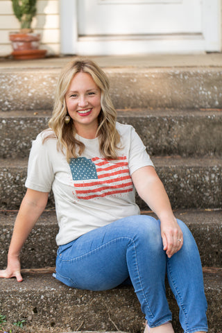 Woman sitting on steps wearing a t-shirt with an American flag design.