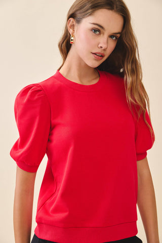 A red knit top featuring a crew neckline, short puff sleeves with gathered shoulders, and ribbed cuffs and hem for a polished fit.