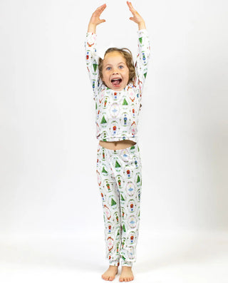 Child wearing a Christmas-inspired Nutcracker Waltz patterned pajama set with arms raised on a white background.