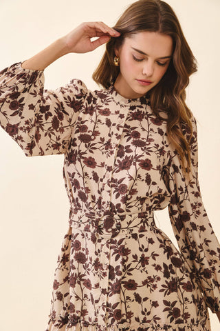 A floral mini dress featuring a high neckline and long puff sleeves with gathered cuffs. Designed with a front button closure and a removable buckle belt to cinch the waist. Finished with a tiered ruffle hem for a feminine, playful touch.
