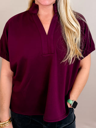 Solid short sleeve top featuring split V-neck with collar band. Elasticated sleeve openings. Back yoke with pleat detail. Unlined. Knit. Non-sheer. Lightweight.