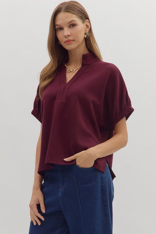 Solid short sleeve top featuring split V-neck with collar band. Elasticated sleeve openings. Back yoke with pleat detail. Unlined. Knit. Non-sheer. Lightweight.