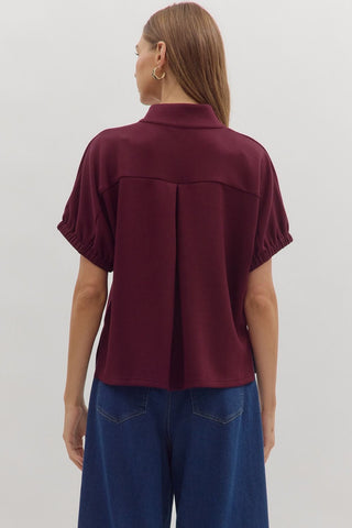 Solid short sleeve top featuring split V-neck with collar band. Elasticated sleeve openings. Back yoke with pleat detail. Unlined. Knit. Non-sheer. Lightweight.